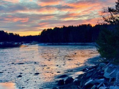 A late winter sunset reflecting in pink, yellow and purple off clouds over a tidal inlet at Crabtree Neck Land Trust's Old Pond Railway Trail